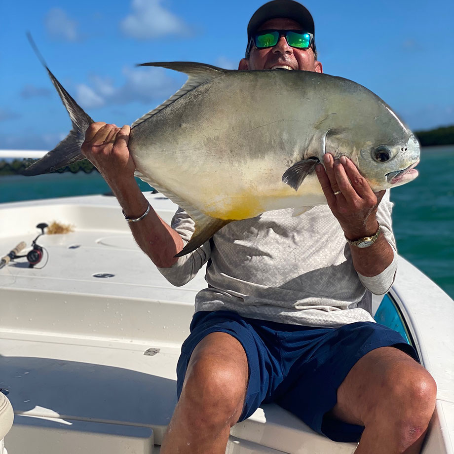 Man on the bow of a boat in sunglasses, smiling while holding a large fish