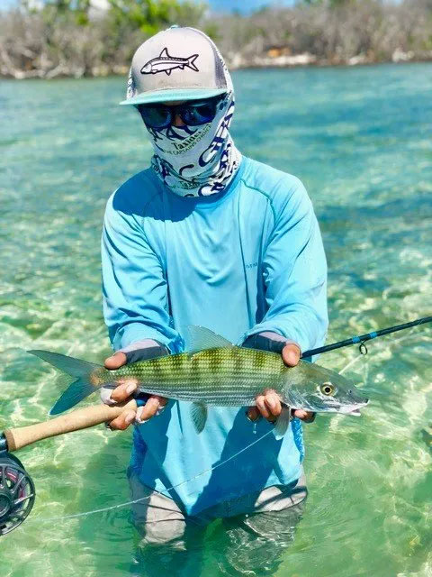 Man standing in waist deep clear water holding fish with hook