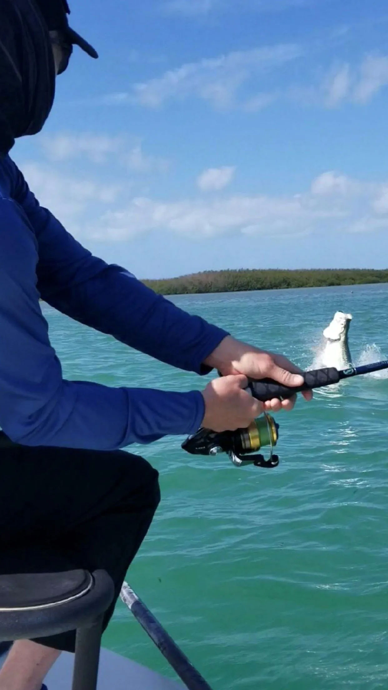 Closeup of fishing reel with fish arching out of the water in the background