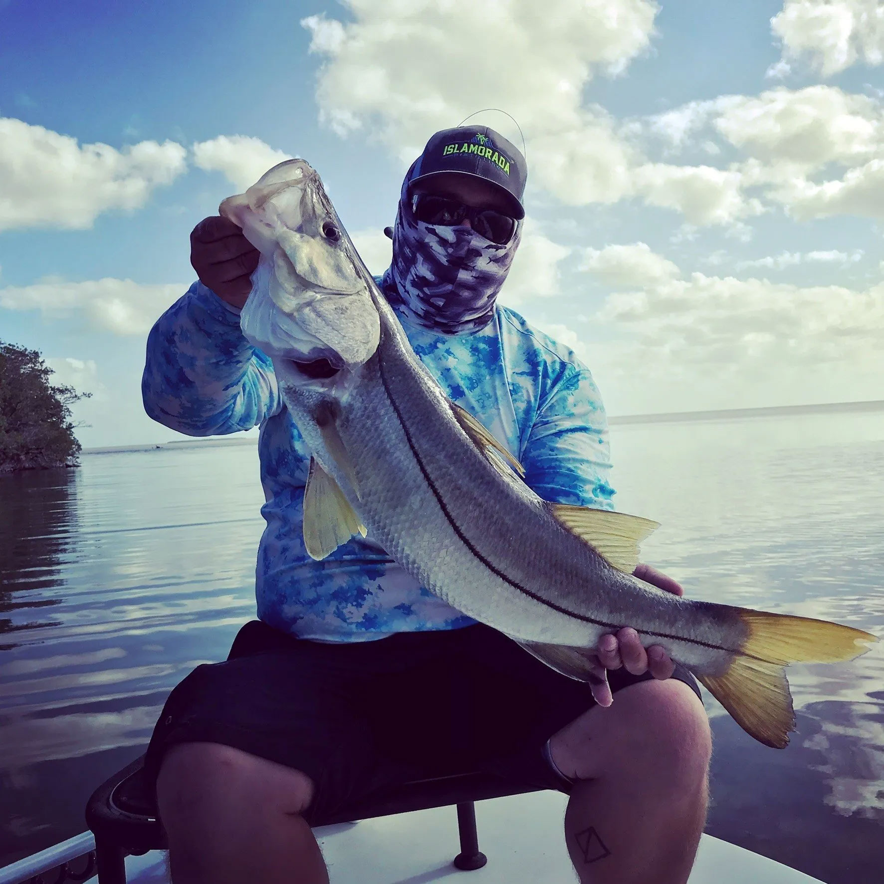 Man in hat, buff and sunglasses holding large trout