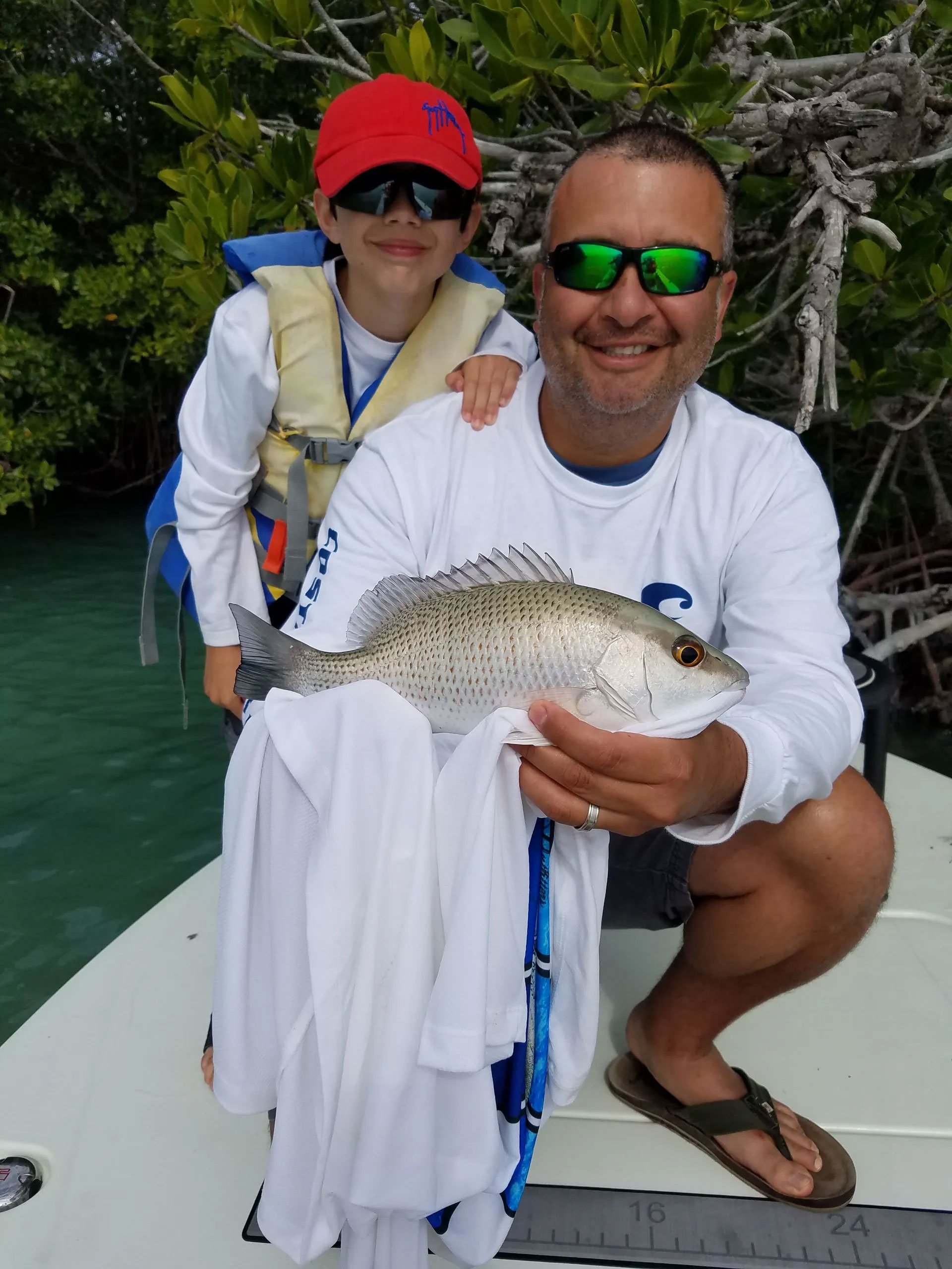 Father kneeling with son, holding fish, smiling