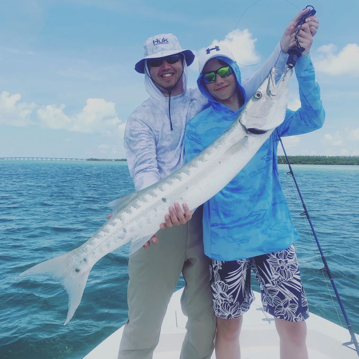 Father and son holding large thin fish together, smiling