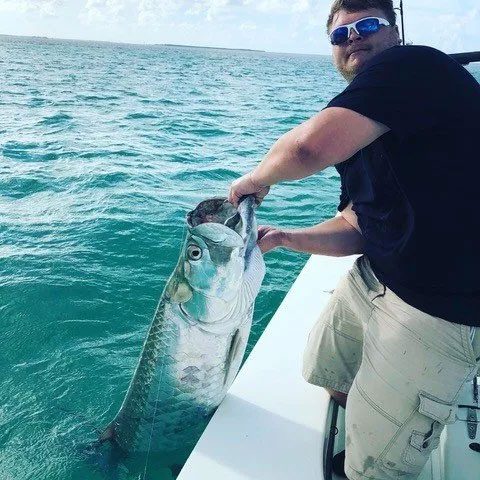 Man holding very large fish over the side of fishing charter boat